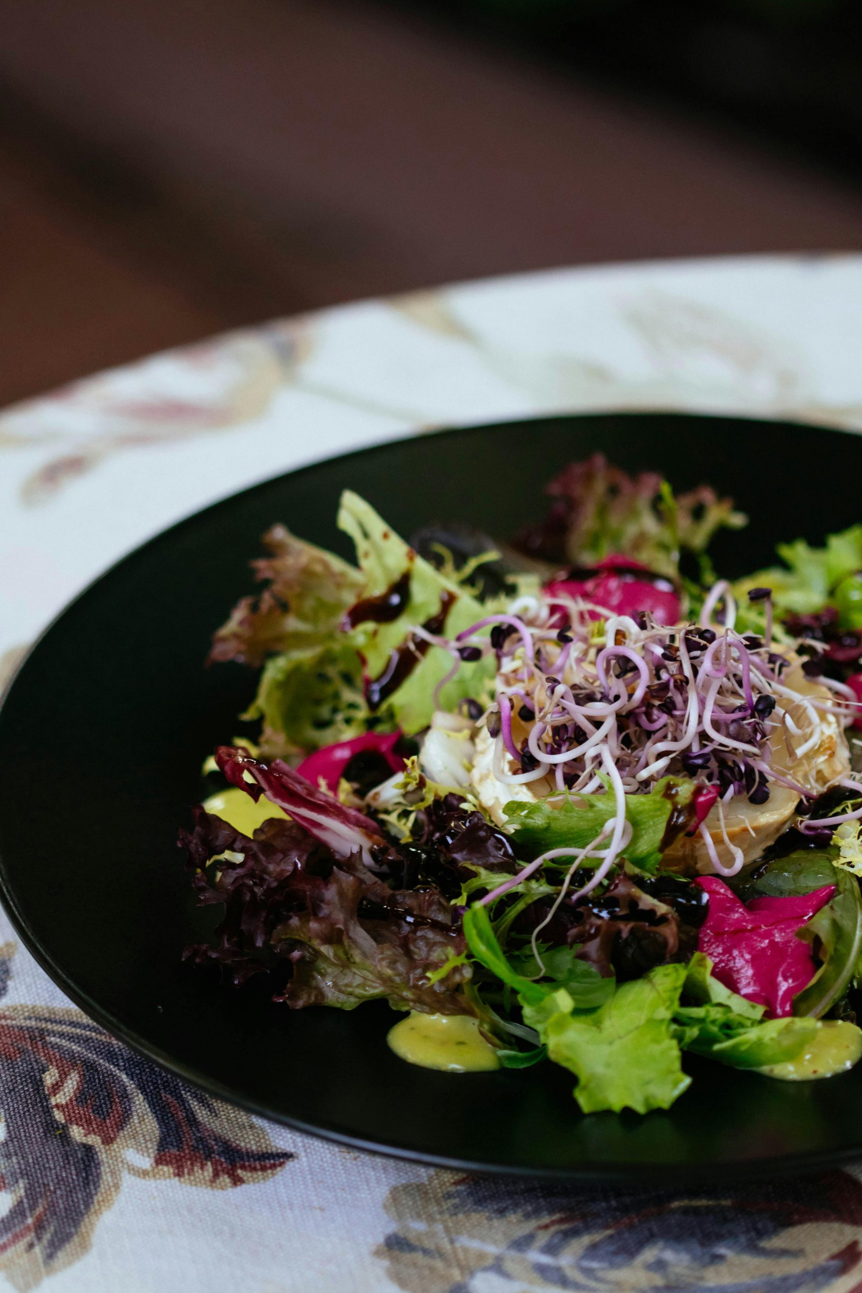 A fresh and colorful mixed green salad garnished with microgreens and dressing.